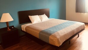 A neatly made bed with a dark headboard, a bedside lamp, and a blue wall. - Troy Inn and Suites (Troy)