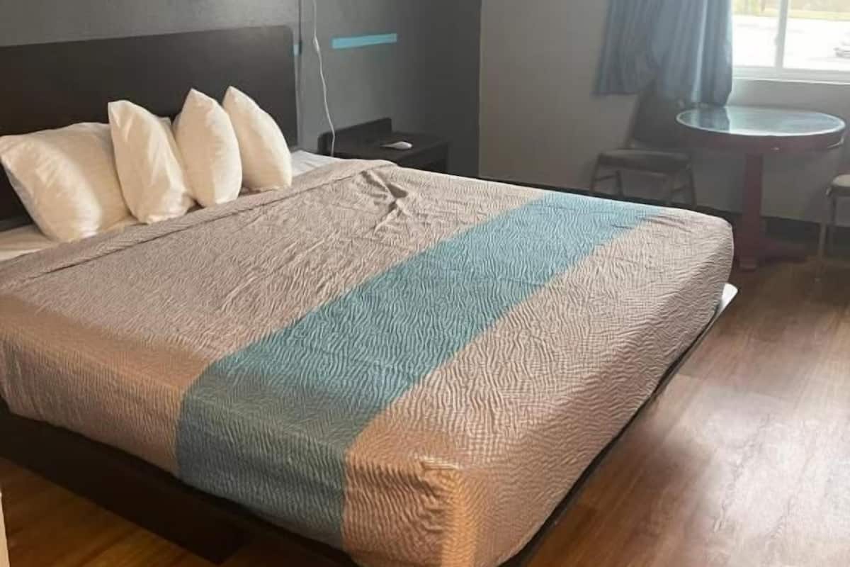 A neatly made bed with a striped blanket, a bedside table with a lamp, and a view of the outdoors through a window with curtains.