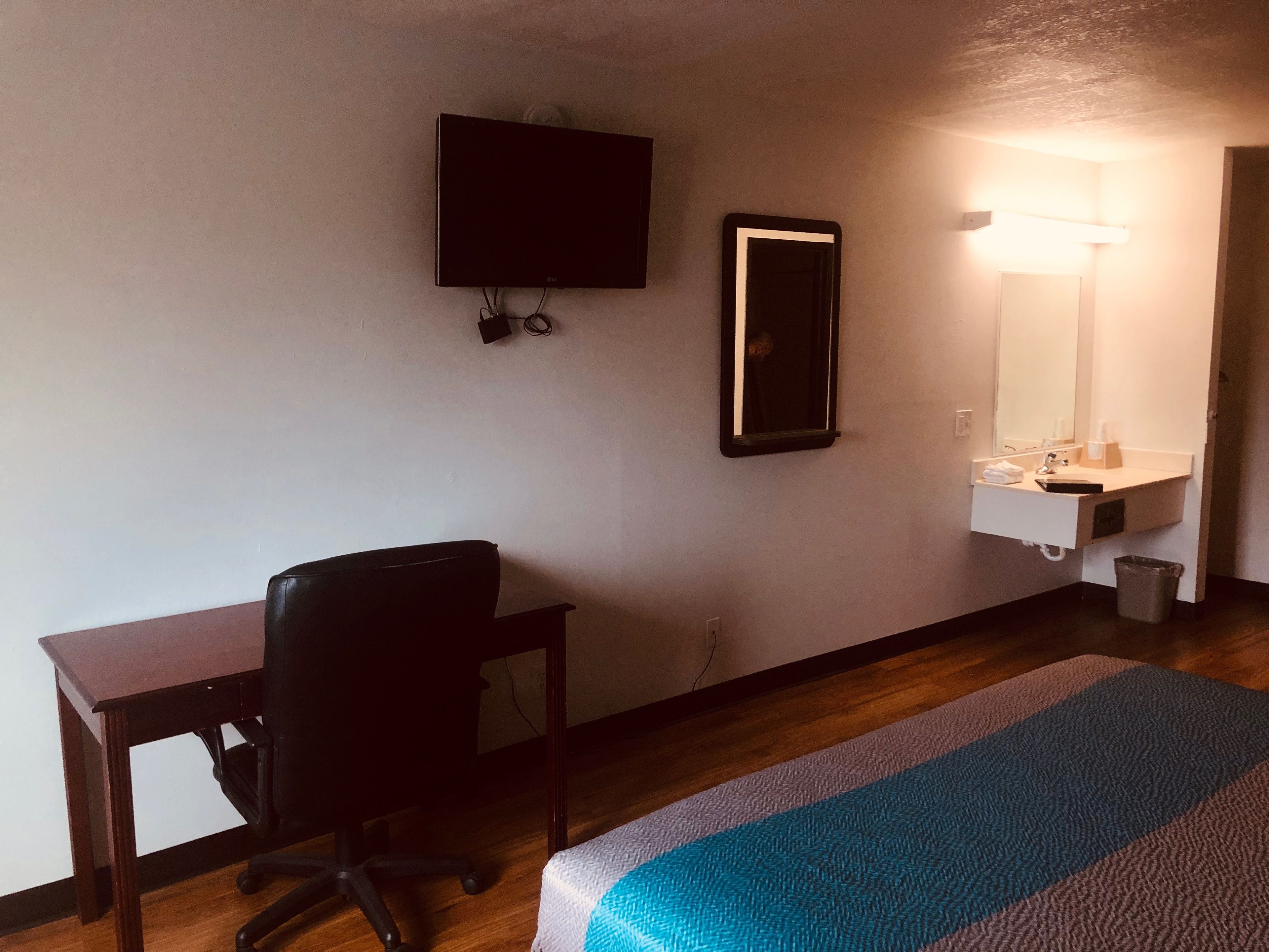 A hotel room with a desk, chair, bed, TV, mirror, and bathroom.