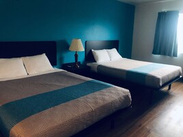 Una habitación de hotel con dos camas, una mesita de noche con lámpara y un ventanal con cortinas.