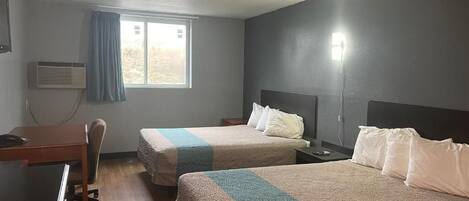 Habitación de hotel con dos camas, un escritorio, una silla y una ventana con cortinas.