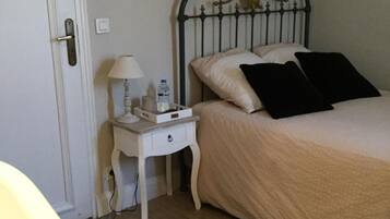 Een slaapkamer met een bed, nachtkastje, lamp en een deur.