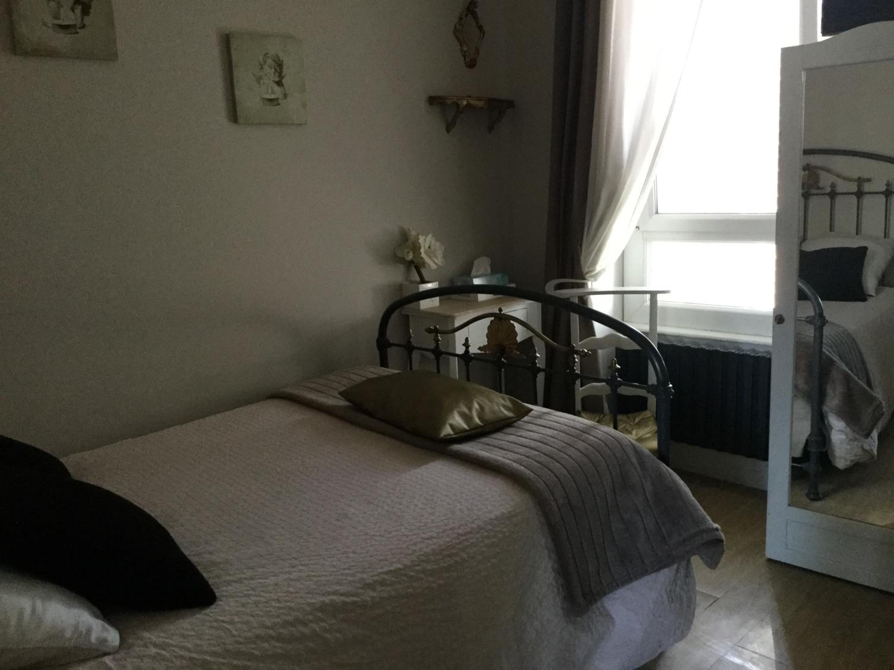 A bedroom with a single bed, a bedside table, a chair, and a window with curtains.