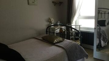 A bedroom with a single bed, a bedside table, a chair, and a window with curtains.