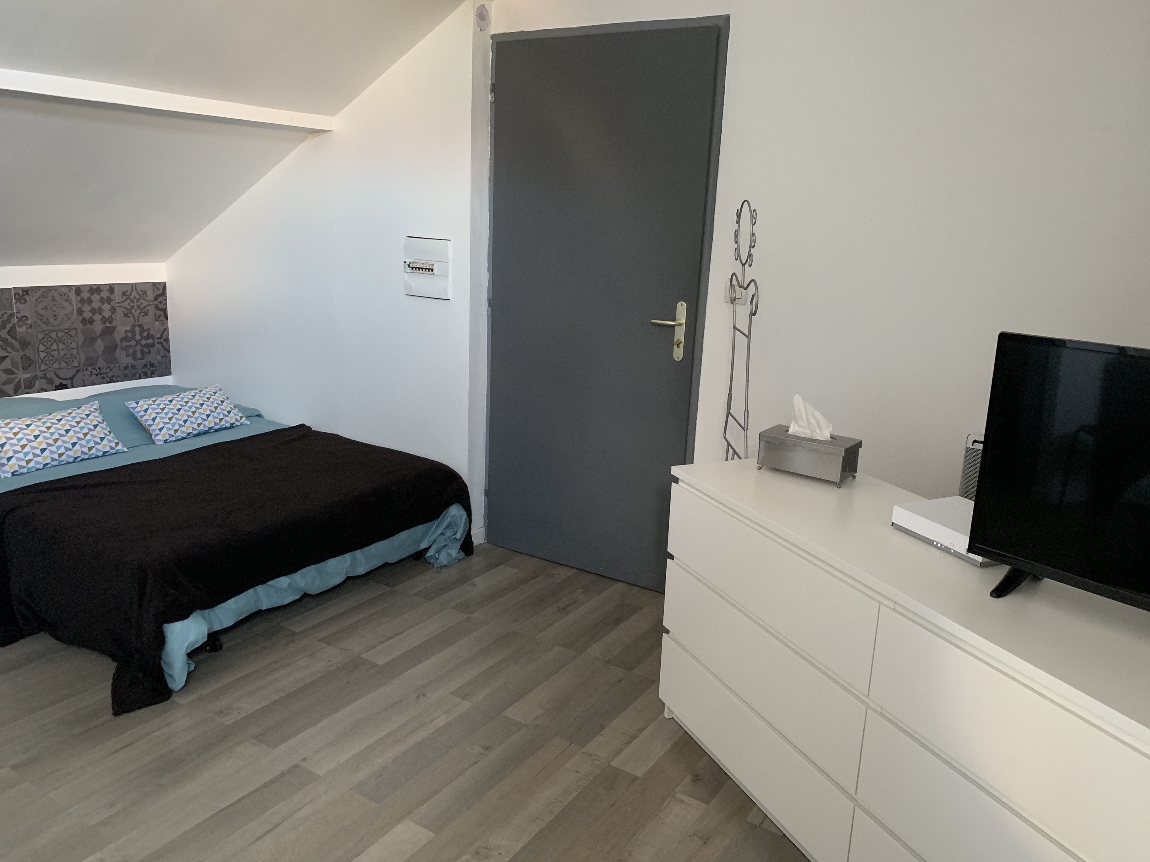 Quarto com cama, cômoda, televisão e porta.