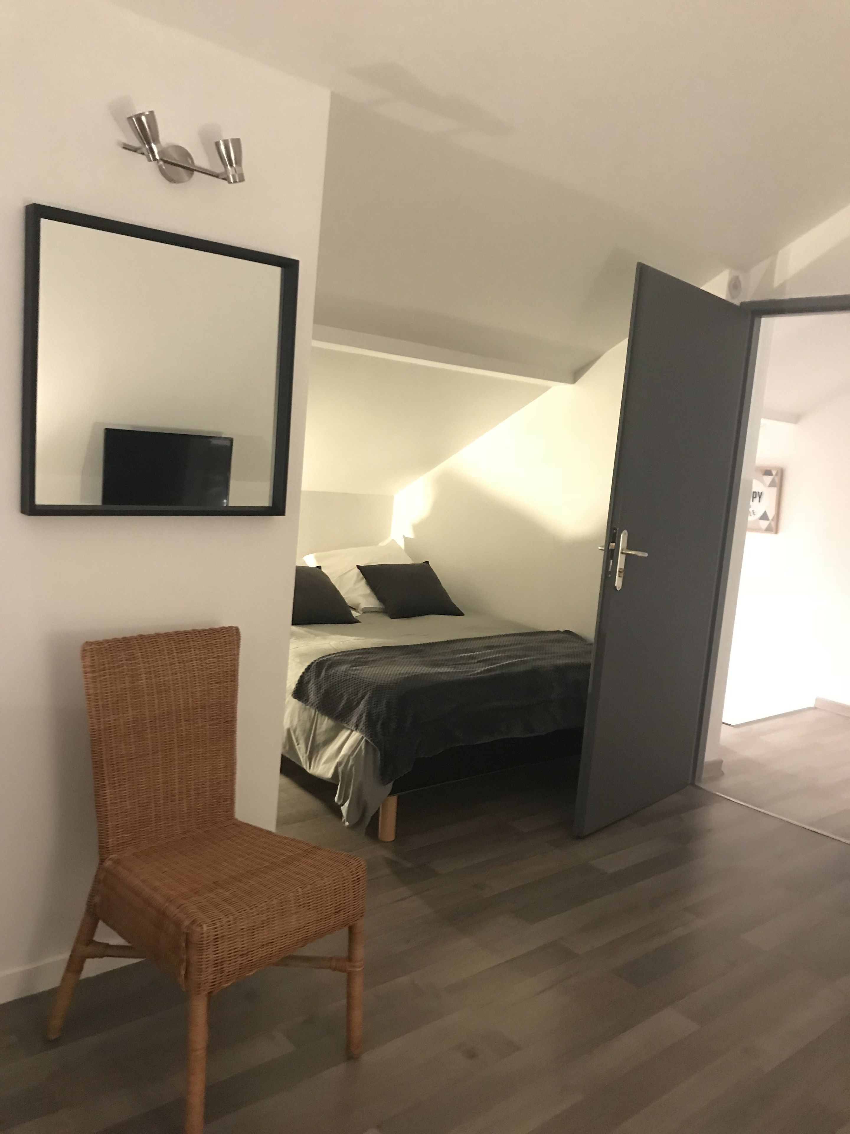 A bedroom with a bed, a chair, a door, and a mirror on the wall.
