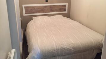 Un dormitorio con cama, cabecera, un pequeño marco de fotos y un radiador.