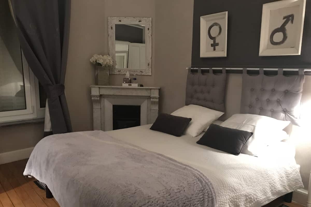 A bedroom with a large bed, a fireplace, and a mirror above it. There are two framed symbols on the wall.