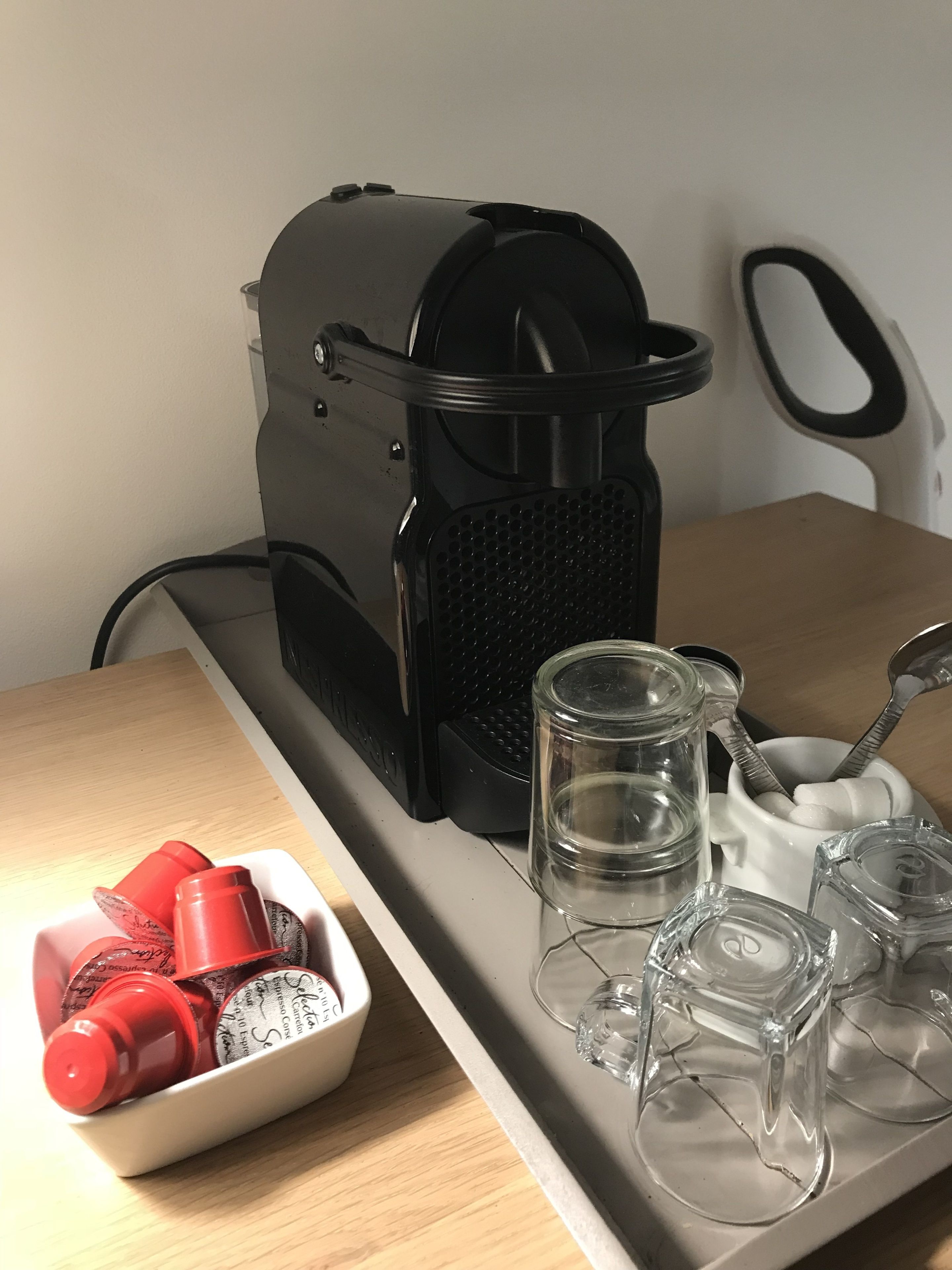 Eine Küchenzeile mit einer Kaffeemaschine, einer Schüssel mit roten Gewürzflaschen und mehreren leeren Gläsern auf einer Arbeitsplatte.