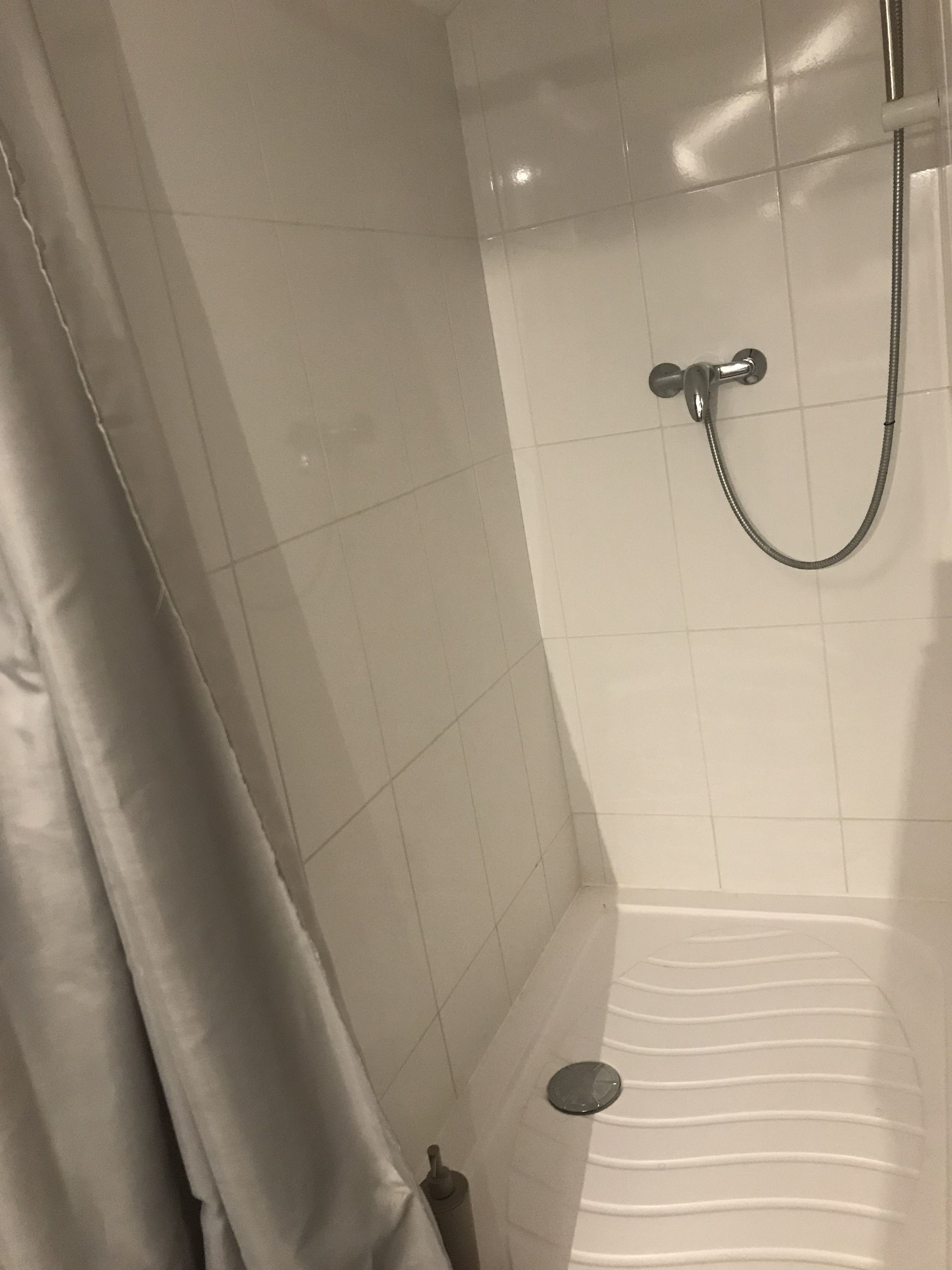 Un espacio de ducha con cortina, un cabezal de ducha manual y desagüe.