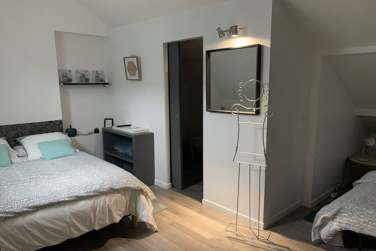 A bedroom with two beds, a bedside table, a wardrobe, a mirror, and a shelf with decorative items.