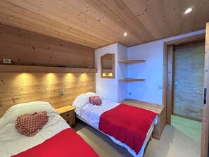 Ein Zimmer mit zwei Betten, Holz-Kopfteilen, einer Holzbank und einer Tür.
