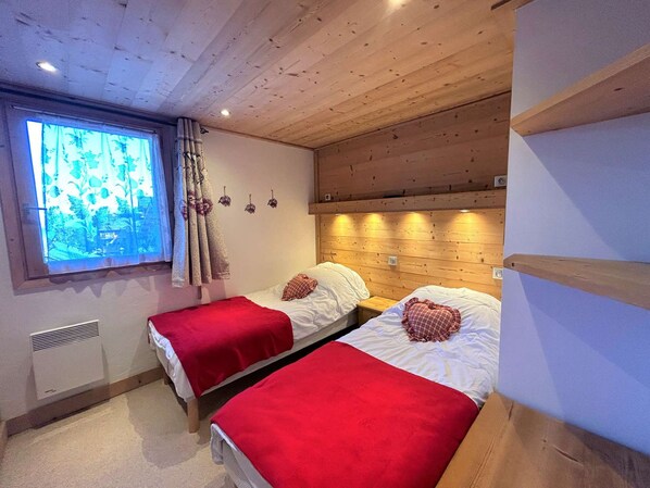 Ein Zimmer mit zwei Betten, jeweils mit roter Decke, Holz-Kopfteil und einem Vorhangfenster.