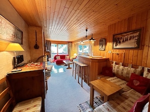 En mysig stuga med träpanel i taket, en matplats, en bar och ett vardagsrum med en röd soffa.