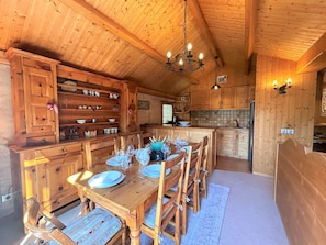 En stuga med träpanel på insidan, med ett matbord för fyra personer, träskåp, en kristallkrona och ett köksområde.