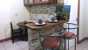 Uma cozinha pequena com painel de pedra, armários de madeira, cafeteira e dois banquetes.