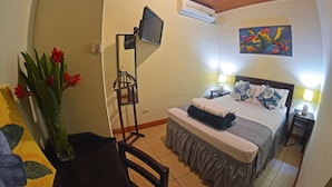 Quarto de hotel com cama, abajures, televisão, pintura e um vaso com flores.