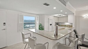 A modern kitchen with a central island, white cabinetry, and a view through the window. - Crystal Sands Tower Unit 509 - Beachfront (SARASOTA)