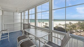 A room with a large window overlooking a beach, a ceiling fan, and a table with chairs. - Crystal Sands Tower Unit 509 - Beachfront (SARASOTA)