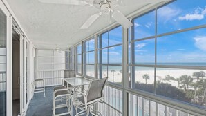 A sunroom with large windows, a ceiling fan, and a table with chairs. - Crystal Sands Tower Unit 509 - Beachfront (SARASOTA)