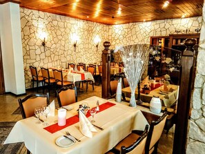 Ein Restaurant mit Steinsäulen, Holzbalkendecke und gedeckten Tischen.