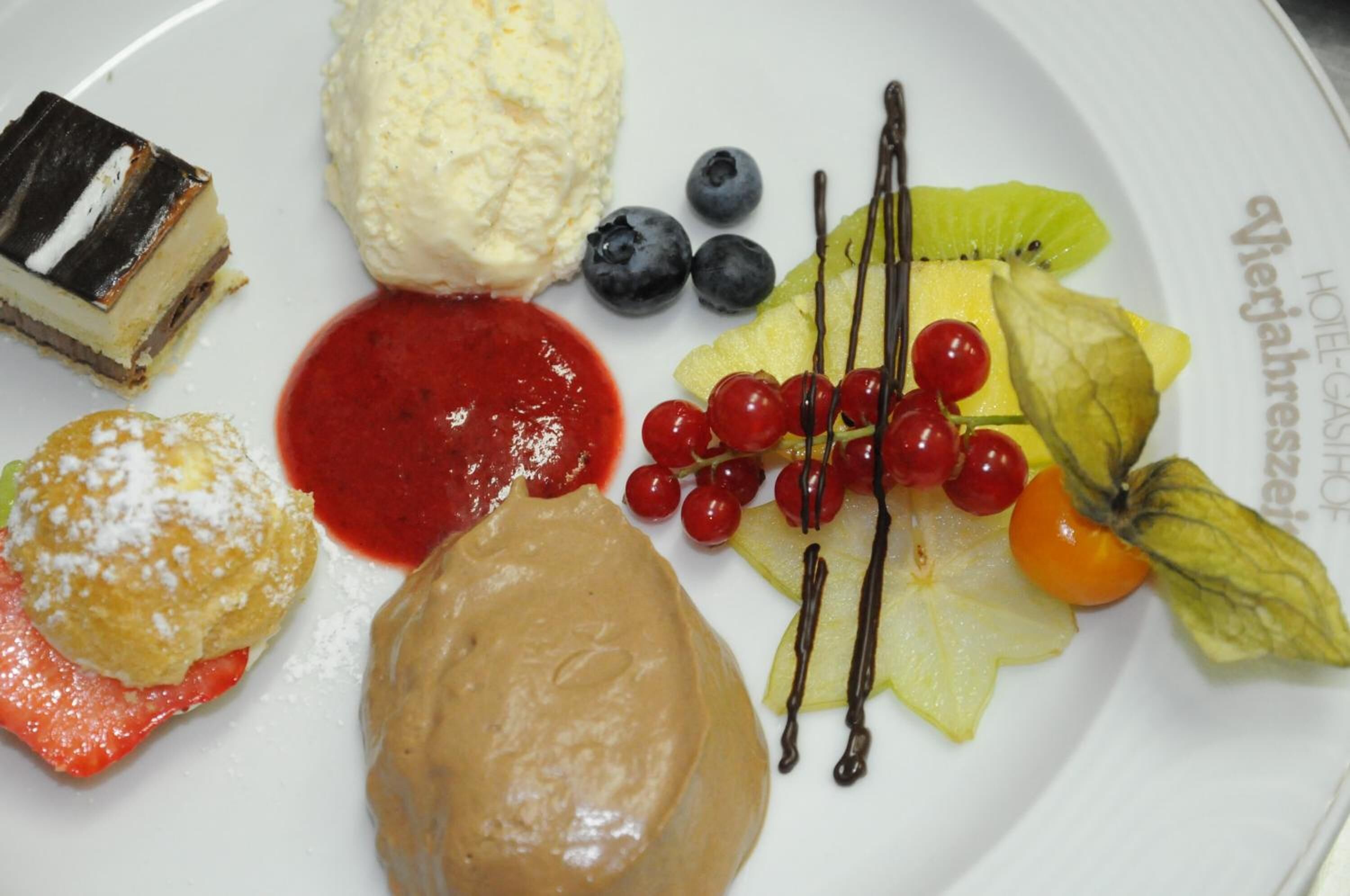 Un plato de postres con varios elementos, como una rebanada de pastel, helado, bayas y una guarnición de frutas.