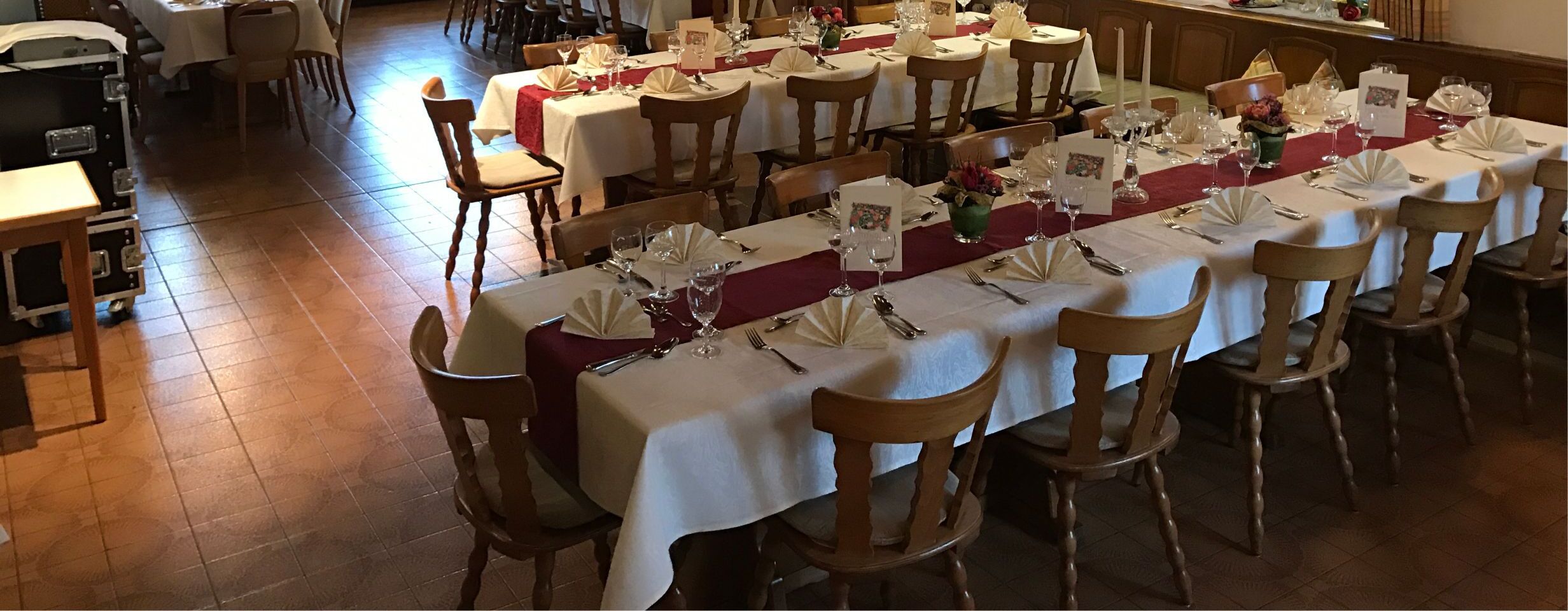 A long dining table set with white tablecloths, red runners, and neatly arranged cutlery.