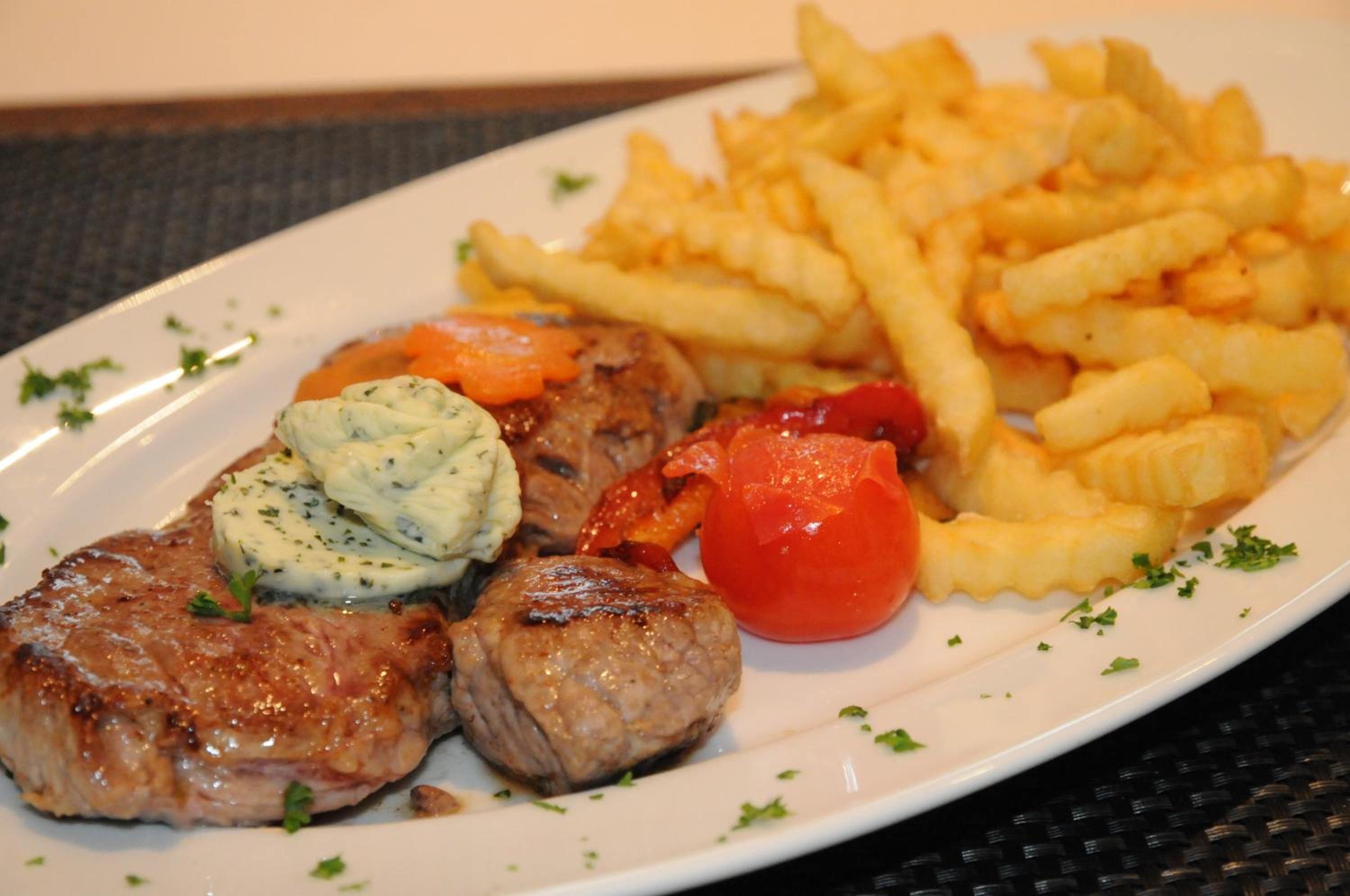 Un plato con carne a la parrilla, tomate y papas fritas.
