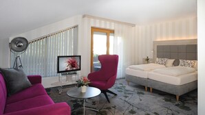 A modern hotel room with a sofa, armchair, and a bed with a headboard.