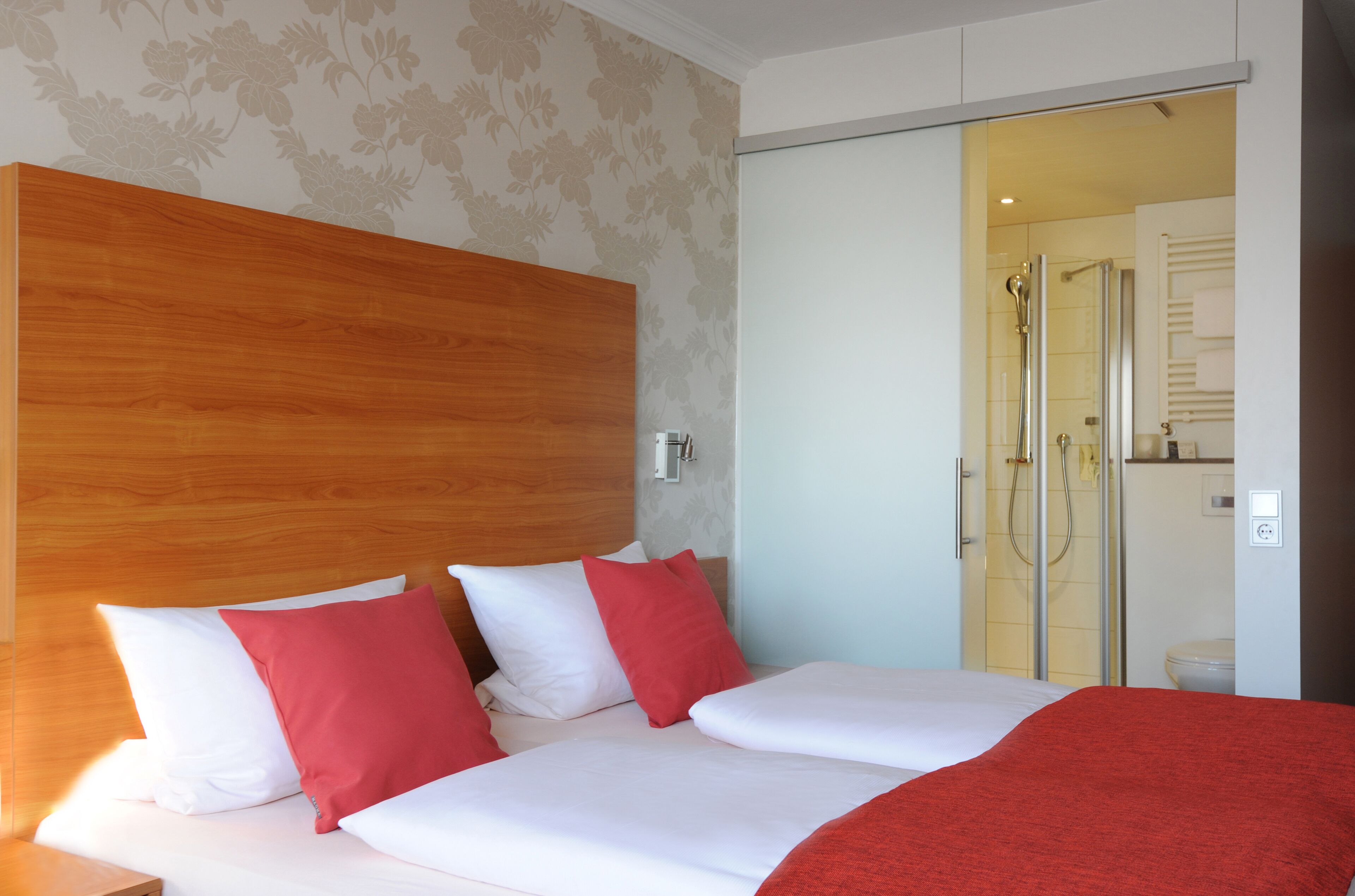 A hotel room with a large bed, a wooden headboard, and a shower area visible through a glass door.