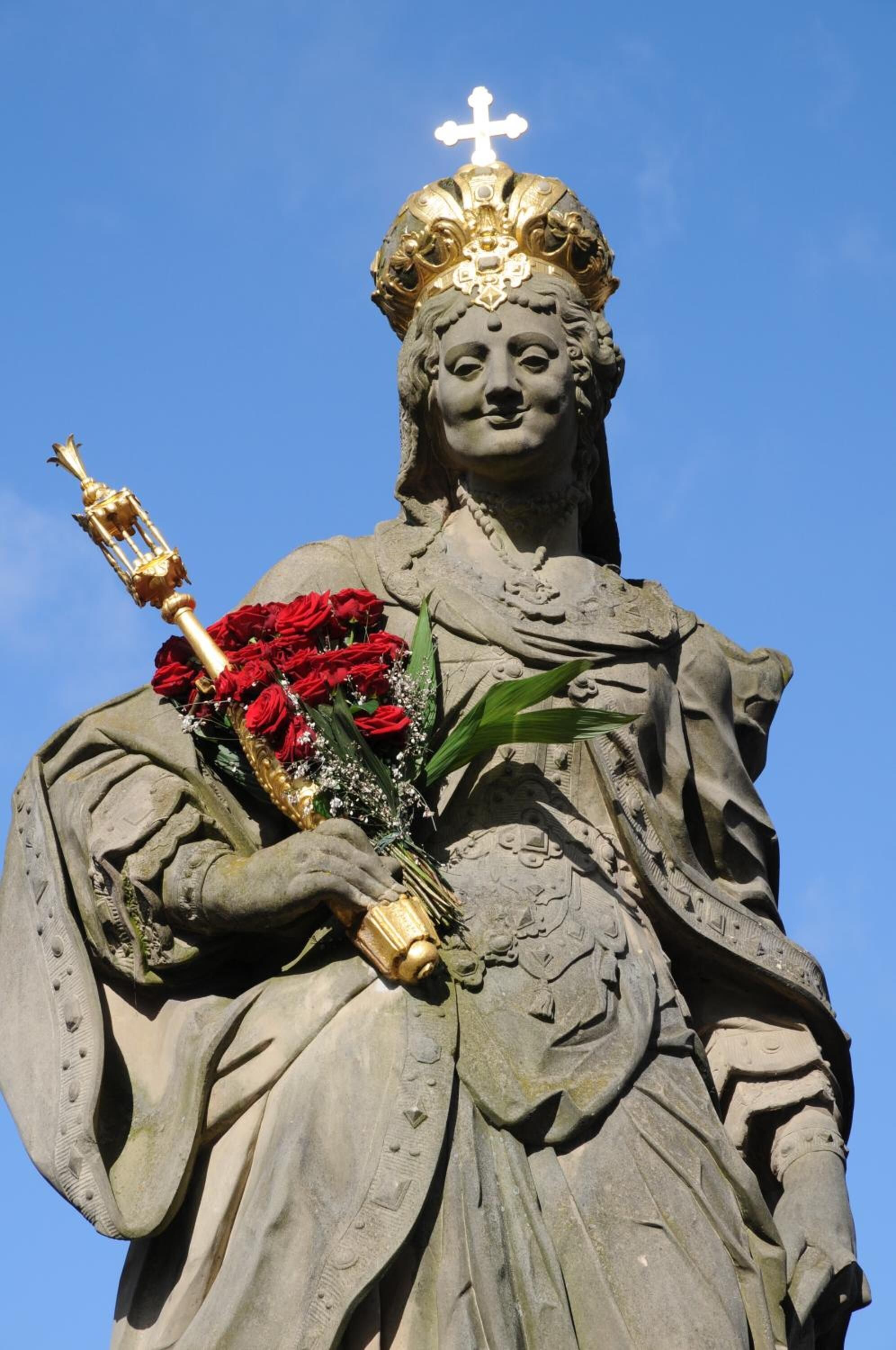 Een standbeeld van een figuur met een boeket rode rozen en een gouden kruis.