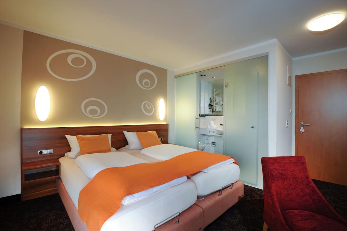 Una habitación de hotel con una cama grande, una silla roja, una mesita de noche de madera y un espejo sobre el tocador.