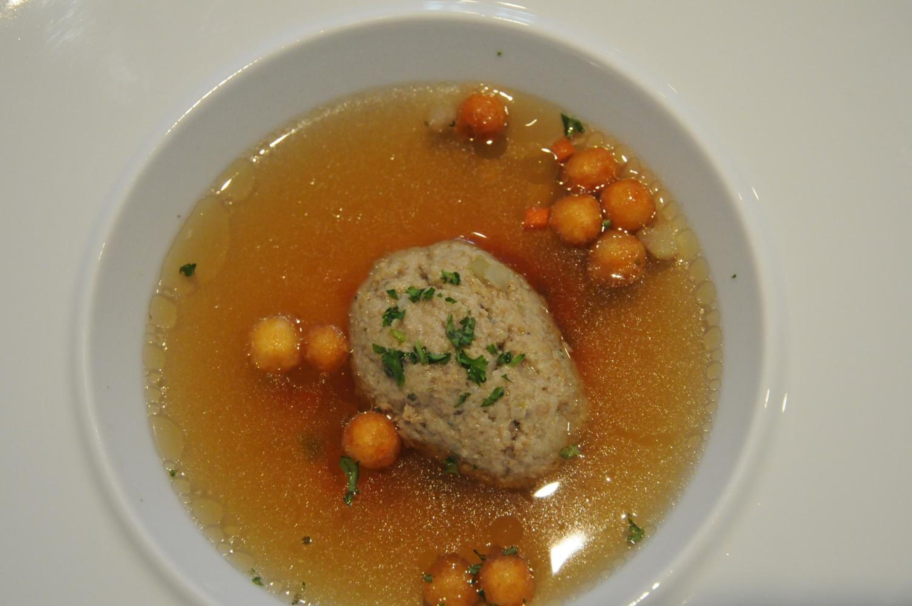 A bowl of soup with a meatball and chickpeas.