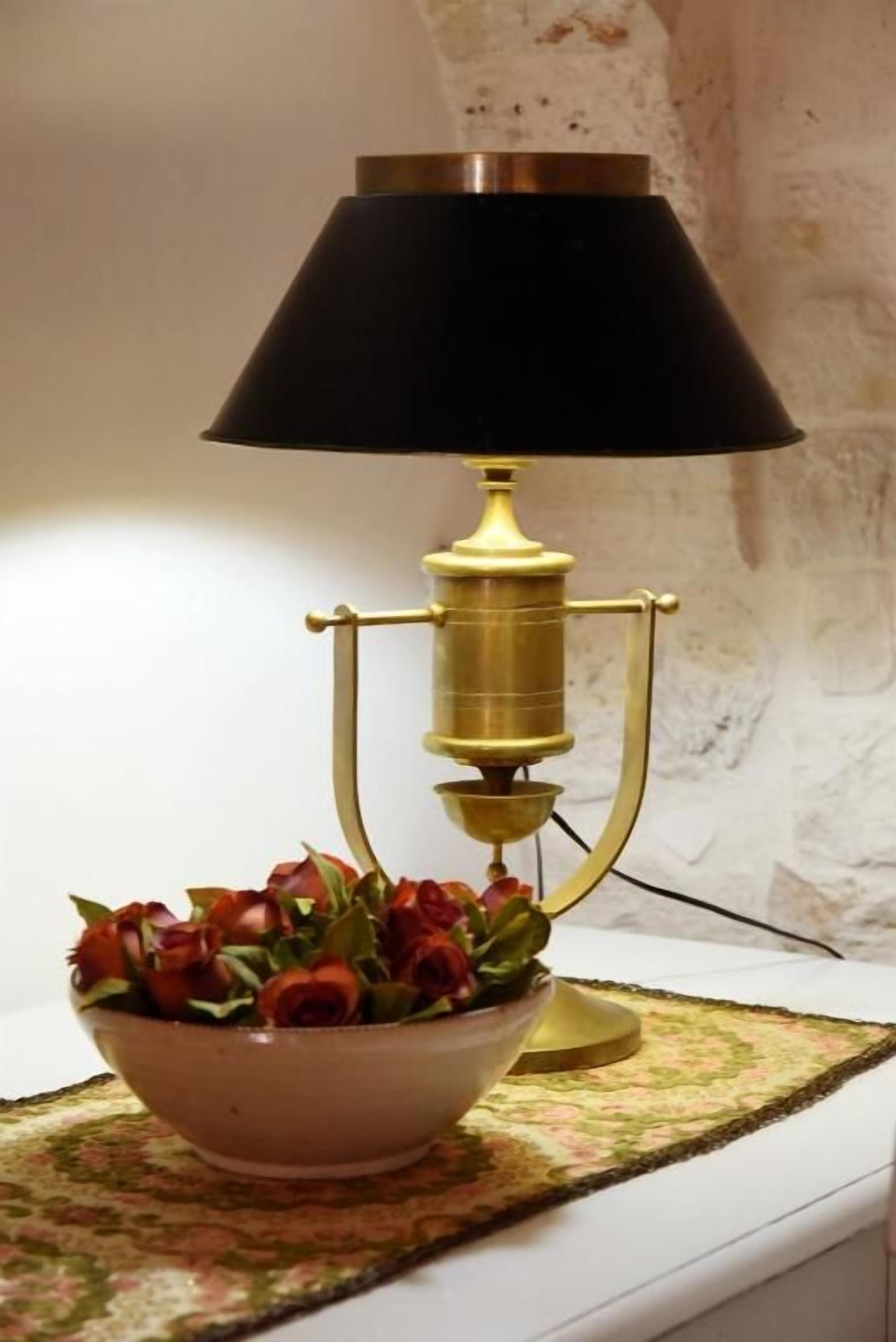 A table lamp with a black shade and brass base, a bowl of red roses, and a patterned tablecloth on a white table.