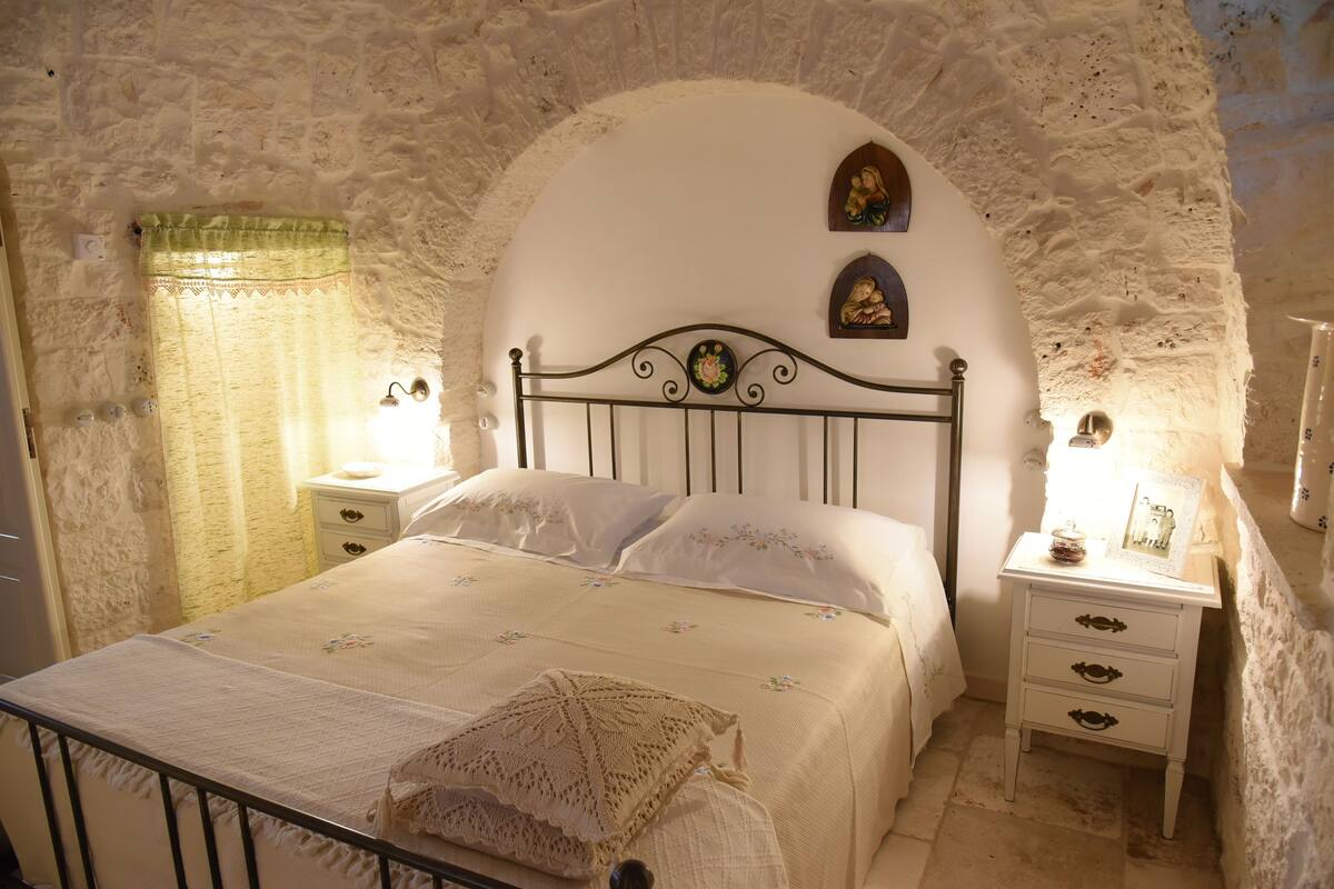A bedroom with a stone wall, a bed with a headboard, two bedside tables, and a nightstand.