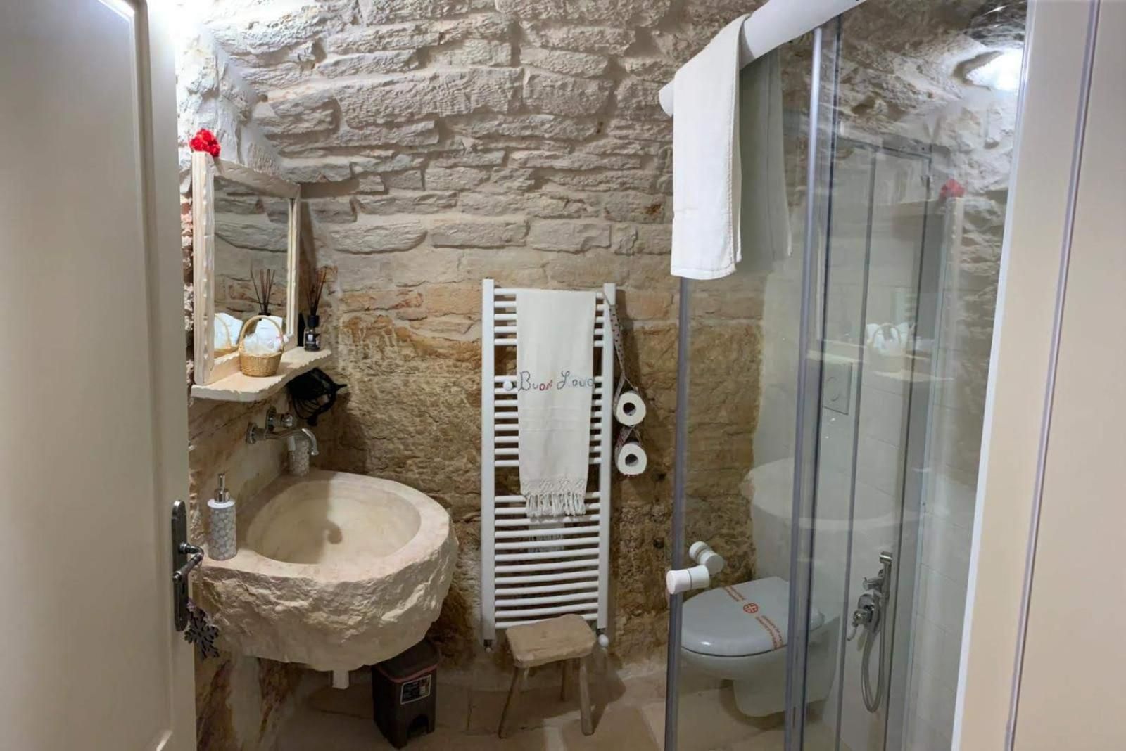 A bathroom with a stone wall, a sink, a towel rack, and a glass-enclosed shower.