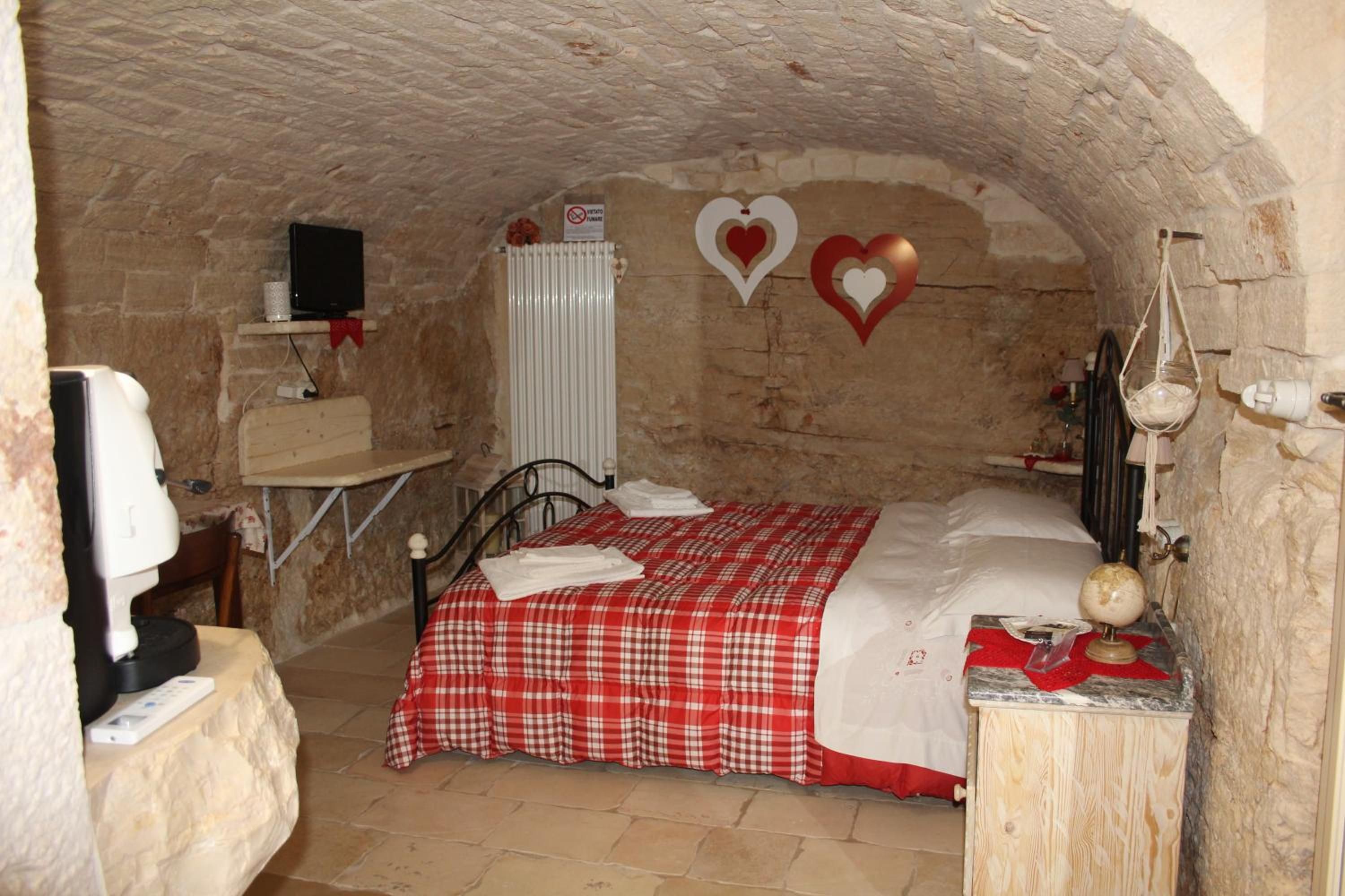 A room with a stone wall, a bed with a red and white checkered bedspread, a white radiator, and a small shelf with a television.