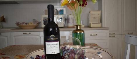 A bottle of Negroamaro wine, a glass, and a plate with grapes on a table in a kitchen setting.