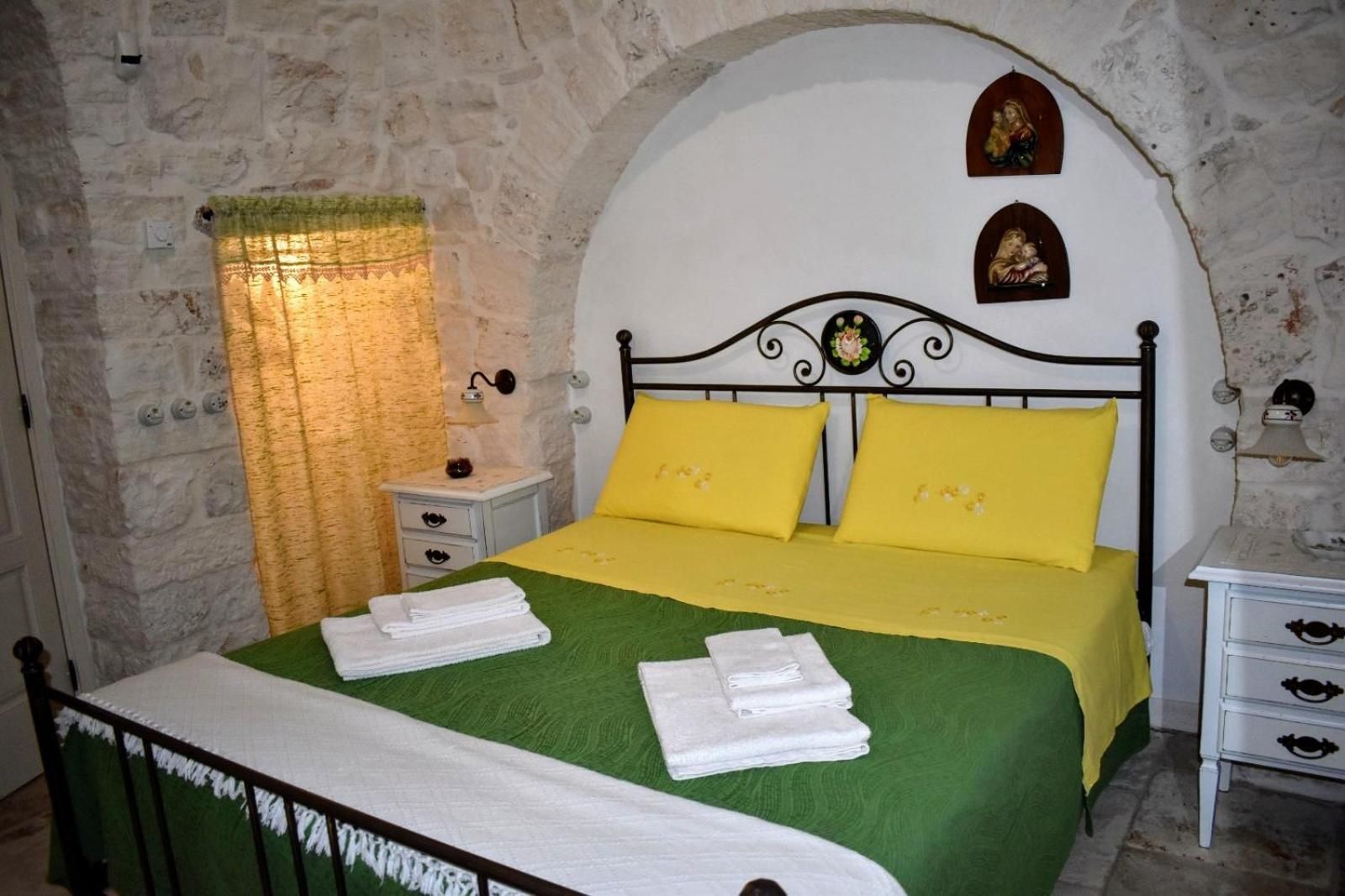 A bedroom with a stone wall, a bed with yellow pillows, a nightstand, and a wall-mounted lamp.