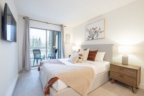 A bedroom with a bed, bedside tables, a TV, and a balcony with chairs.