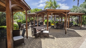 Un espace extérieur aménagé en terrasse, avec des pergolas en bois, des meubles en osier et un sol pavé.