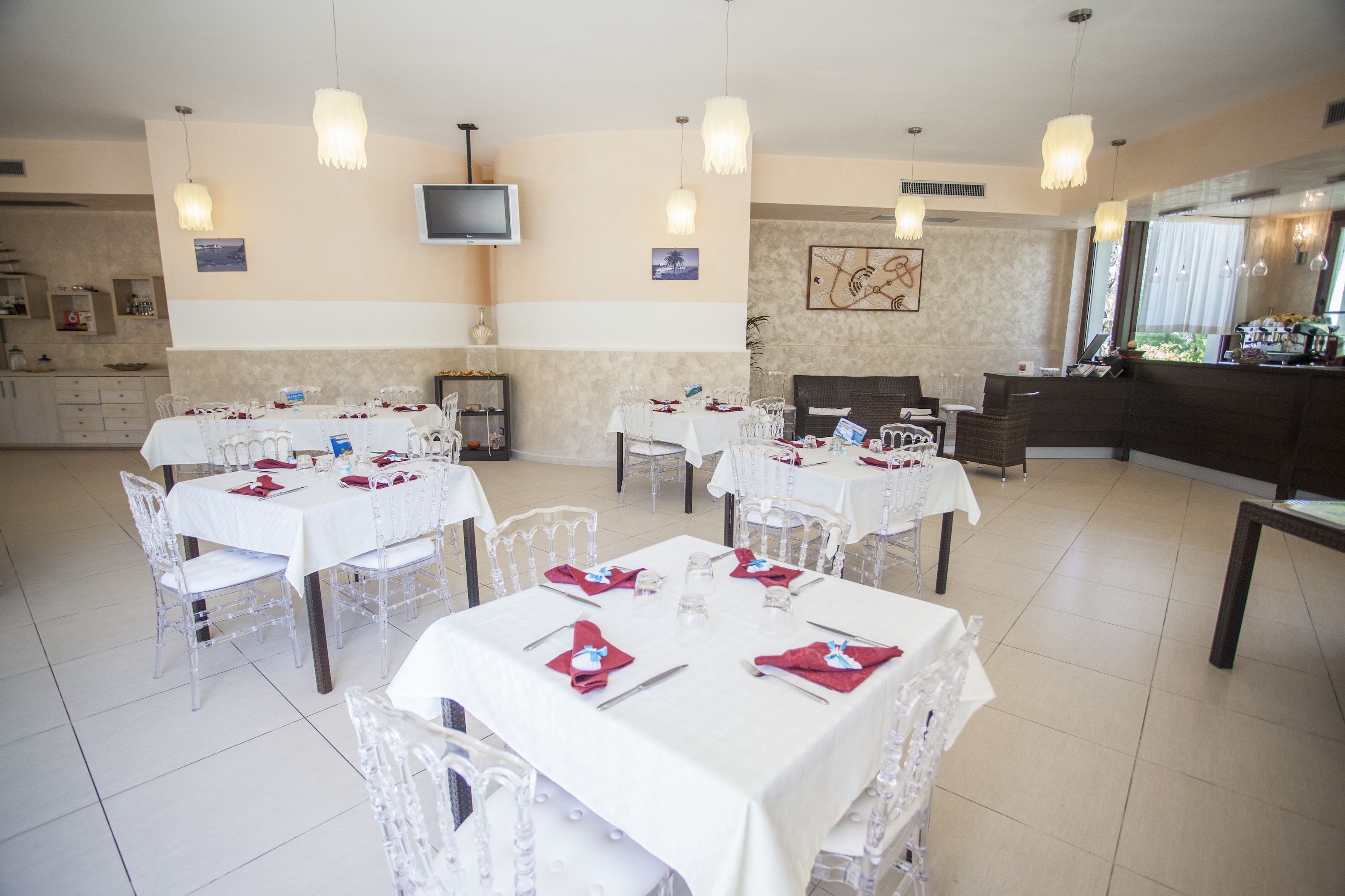 Un espace repas avec plusieurs tables dressées pour un repas, un téléviseur fixé au mur et, au fond, un coin cuisine.