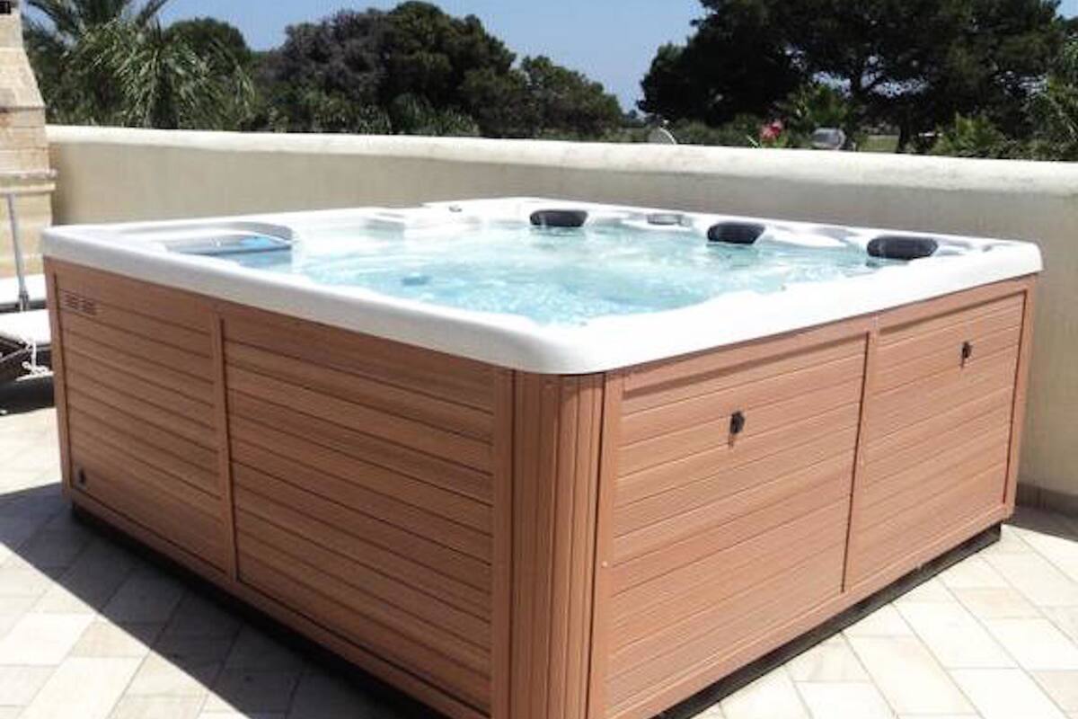 A rectangular hot tub with wooden panels and a white edge, placed on a tiled patio.