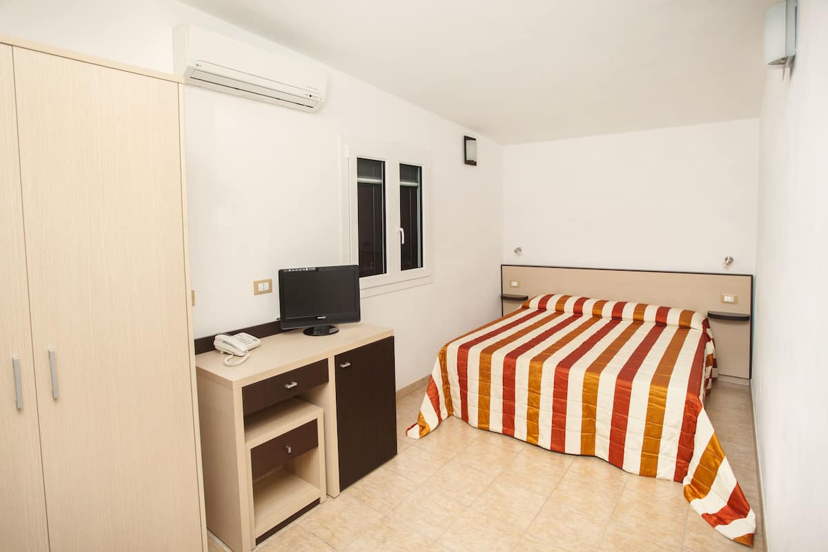 A bedroom with a bed, a desk with a computer, a wardrobe, and a window.