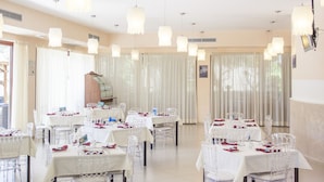 Un vaste espace dédié à la salle à manger, avec de nombreuses tables et chaises, de grandes fenêtres dotées de rideaux et un éclairage suspendu.