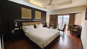 A modern hotel room with a large bed, a desk, and a balcony with a view of the city. - The Oasis -Vadodara  (Vadodara)