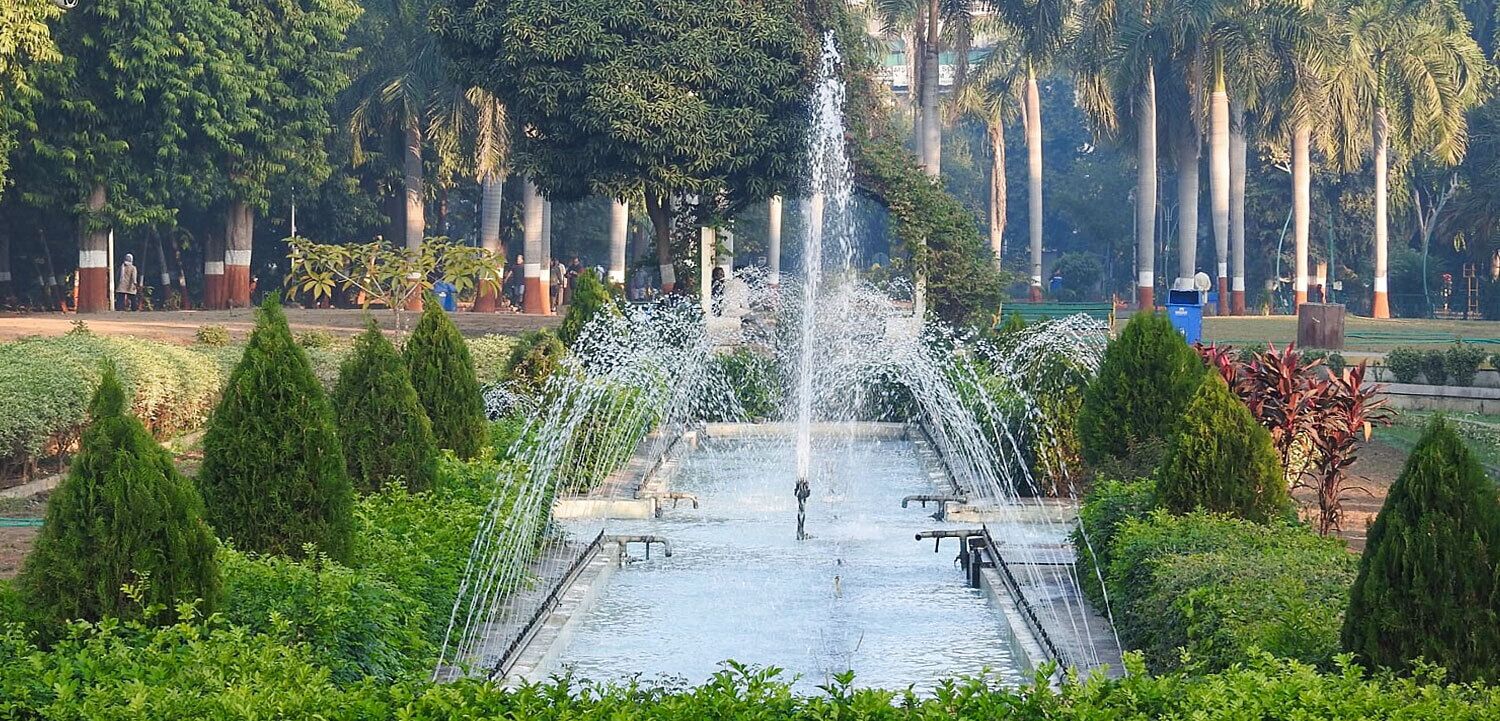 Una fuente en un parque con árboles y una persona caminando cerca.