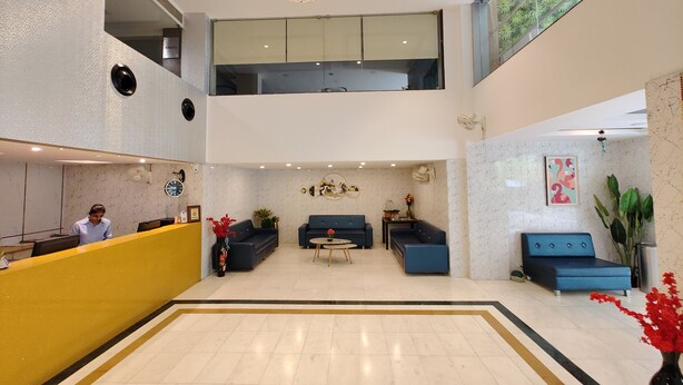 A spacious lobby with a reception desk, sofas, a chandelier, and a large window. - The Oasis -Vadodara  (Vadodara)