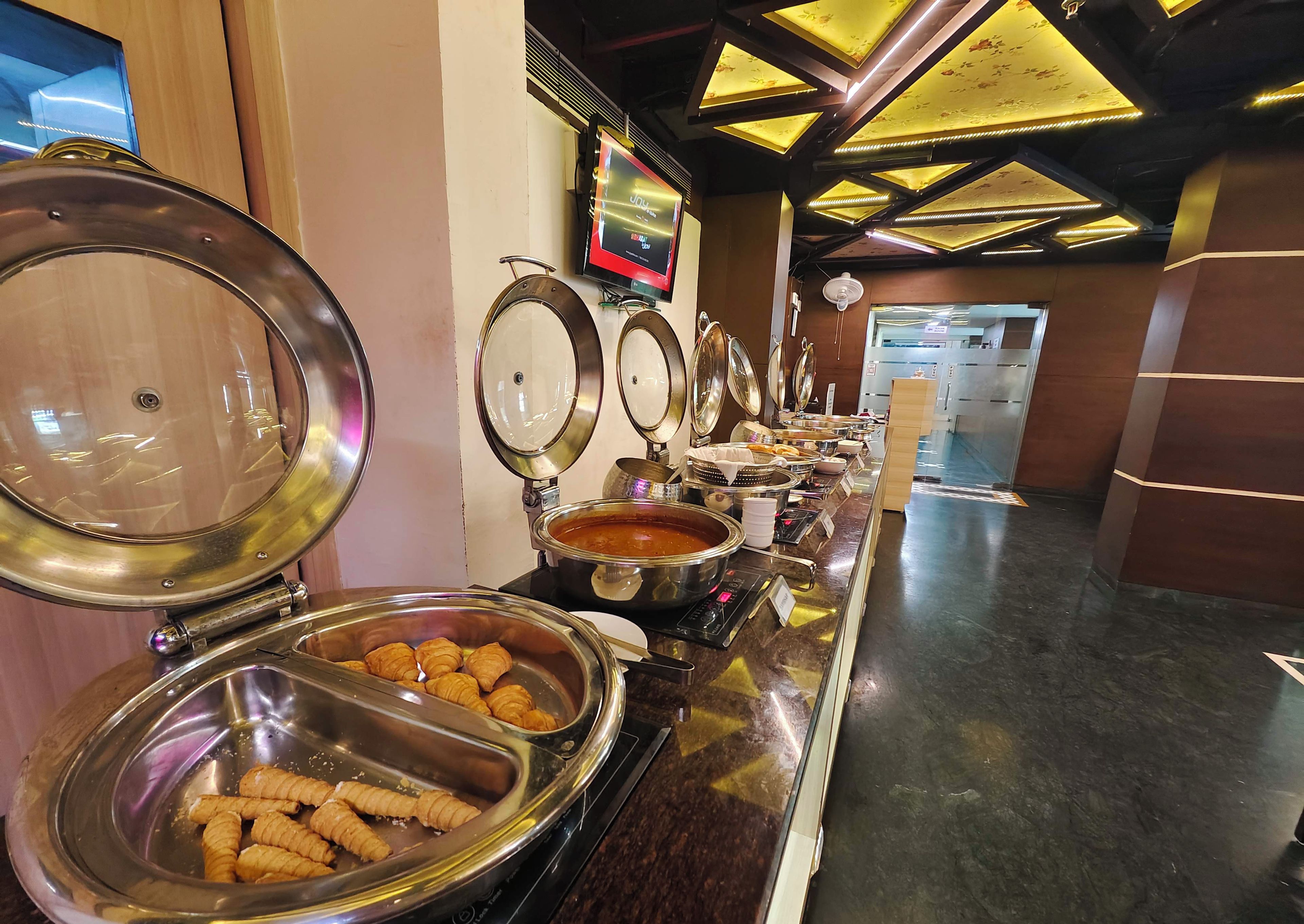 A buffet line with various food items and a television screen in the background.