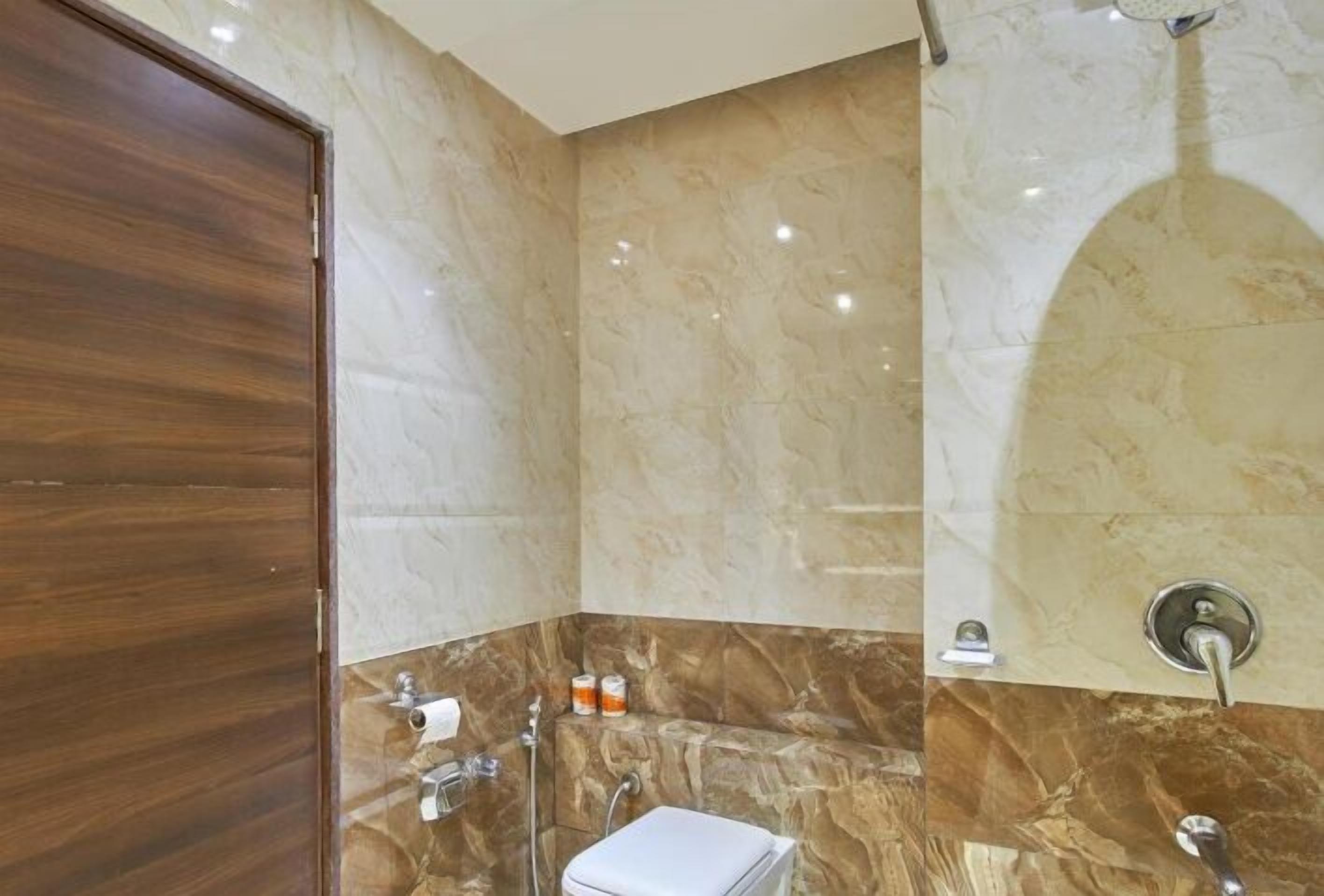 A bathroom with a wooden door, marble walls, a white toilet, and a shower area.